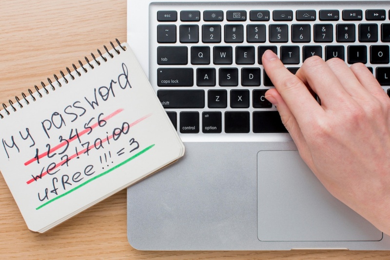 A person typing on a laptop, which sits next to a notepad