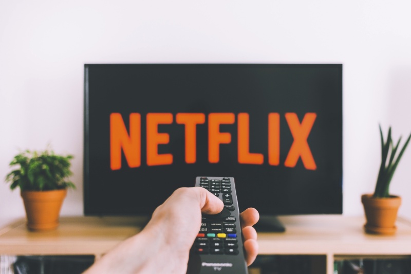 A person holding a remote control and pointing it to a TV screen on which there is Netflix logo