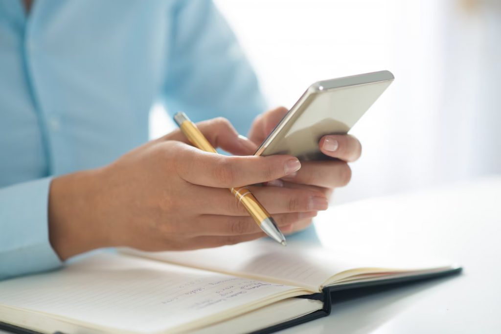 A person holding a pend and using a smartphone